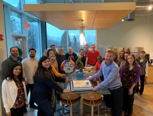 employees gather around a cake celebrate